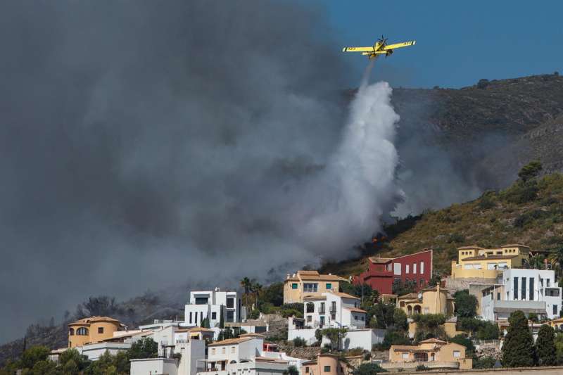 Una avioneta realiza una descarga de agua sobre las llamas que avanzan hacia una zona de viviendas en la Atzubia. EFE/Natxo FrancÃ©s
