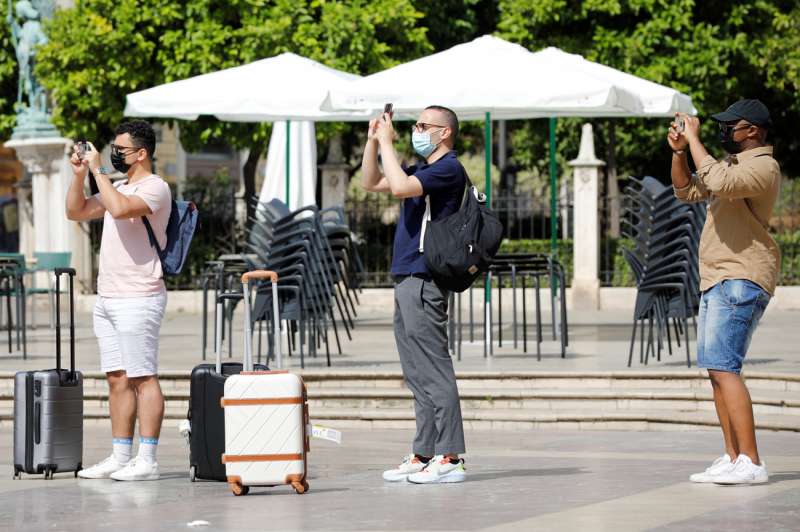 Tres turistas cargados con sus maletas realizan una foto en la plaza de la Virgen. /EFE /Ana Escobar